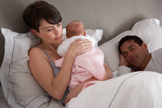 Mother Cuddling Newborn Baby In Bed At Home